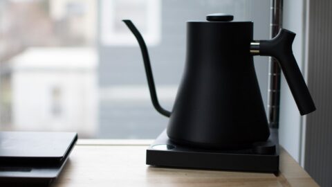 A black gooseneck kettle pouring a thin stream of water into a white ceramic V60 dripper with coffee grounds