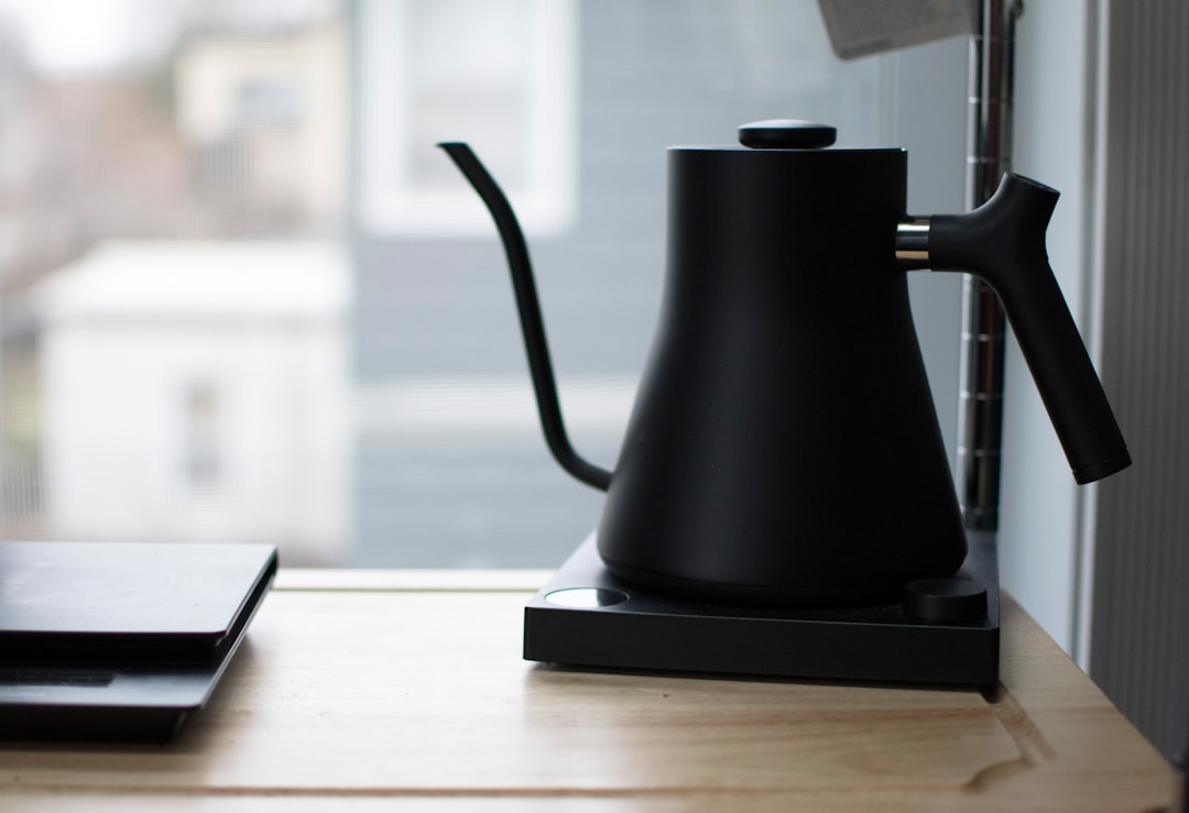 A black gooseneck kettle pouring a thin stream of water into a white ceramic V60 dripper with coffee grounds