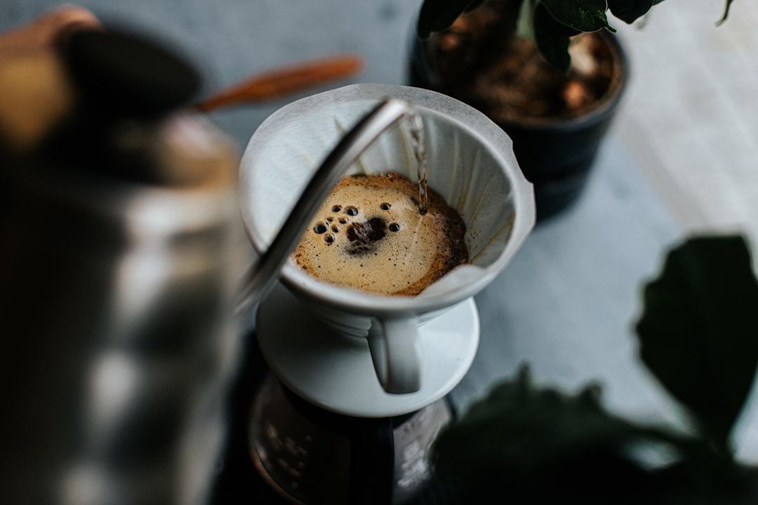 A close-up of a ceramic pour-over dripper with dark, coarse decaf coffee grounds, steam rising from the cup, focusing on the texture of the decaf grounds.